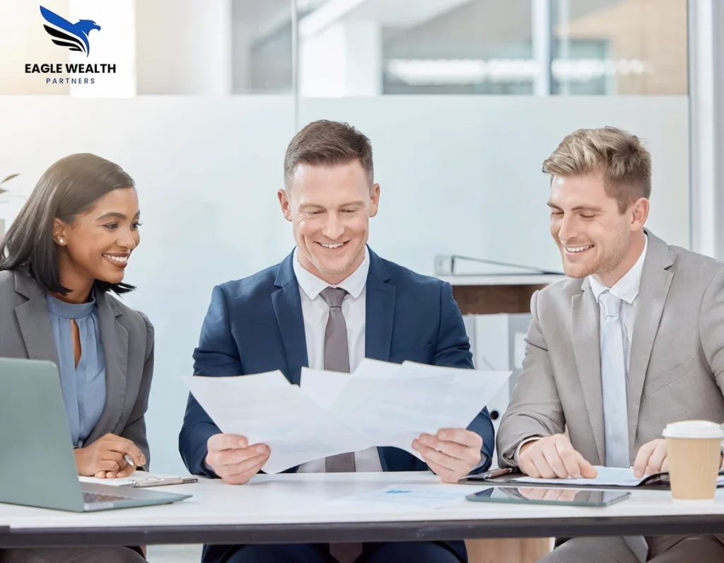 Three business professionals smiling while reviewing documents together in an office